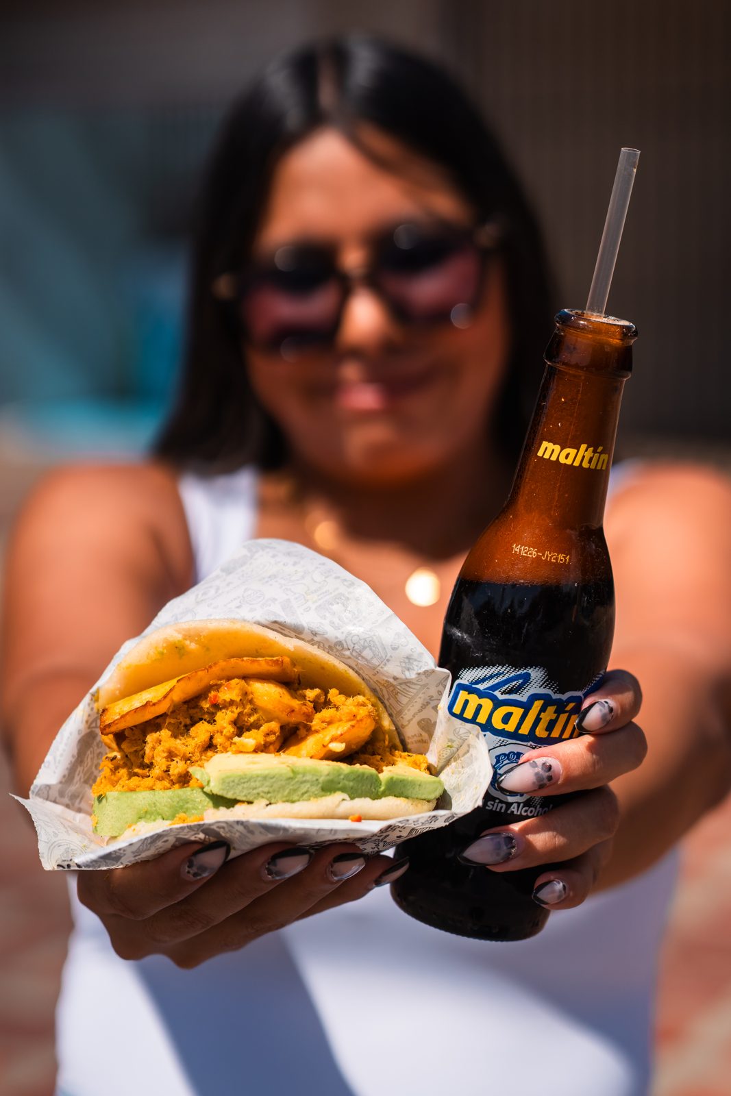 Clienta sonriendo con su arepa y su malta